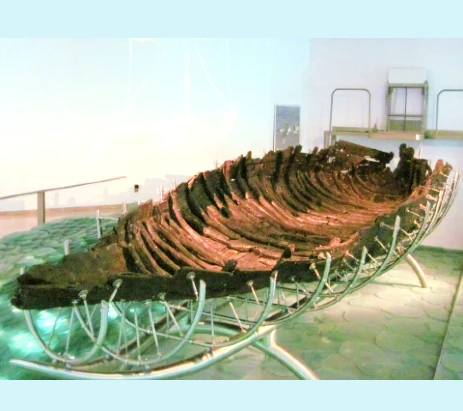 Jesus boat picture of a boat in a museum that's very shallow, mostly wooden ribs, propped up by a metal frame